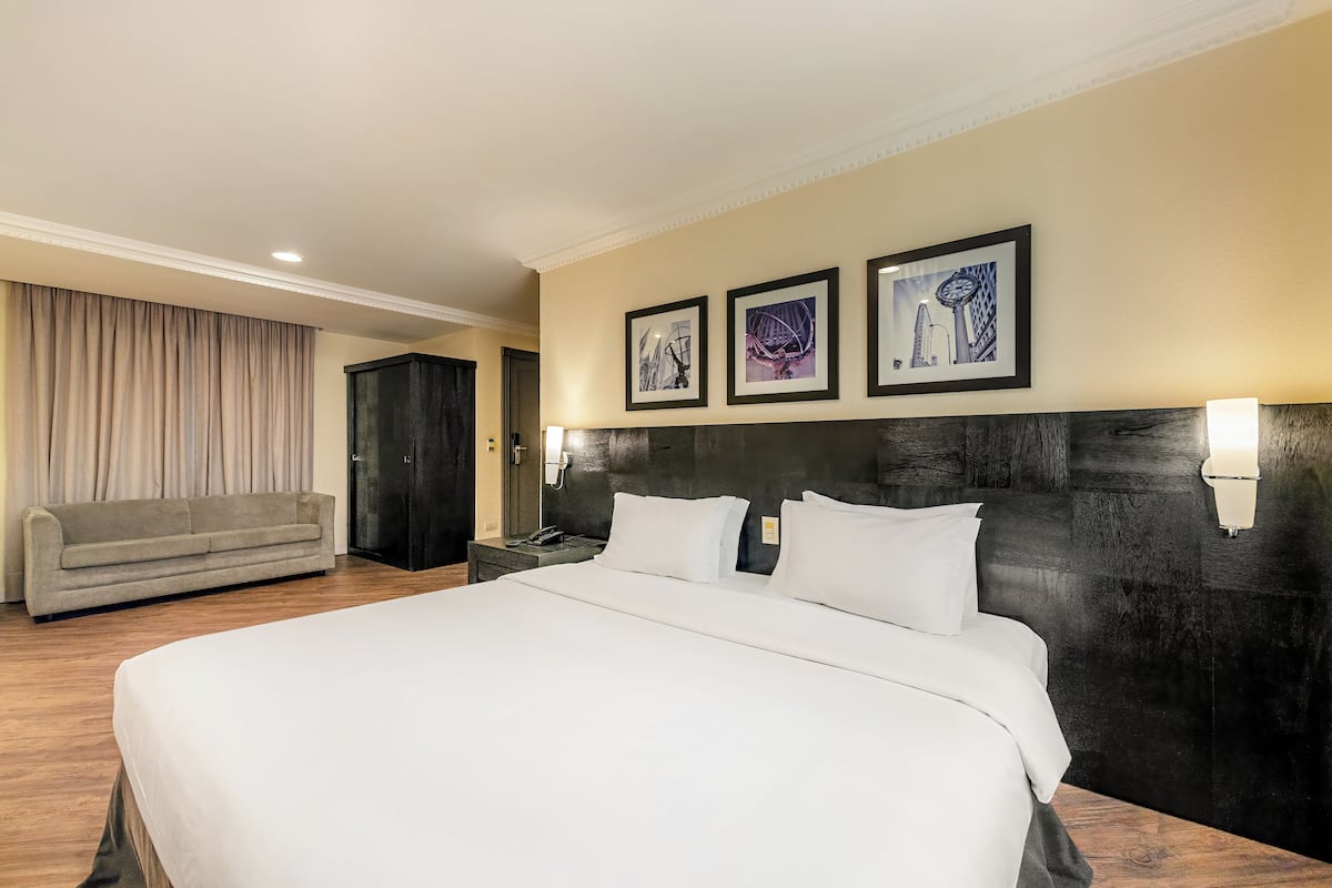 A hotel room with a large bed, a sofa, and three framed pictures on the wall.