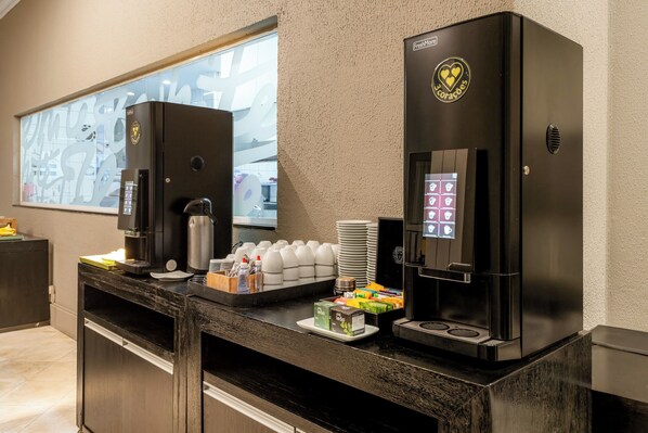 Un espace dédié au café, équipé de deux machines à café, d’une pile de gobelets jetables et d’un assortiment de produits pour le petit-déjeuner.