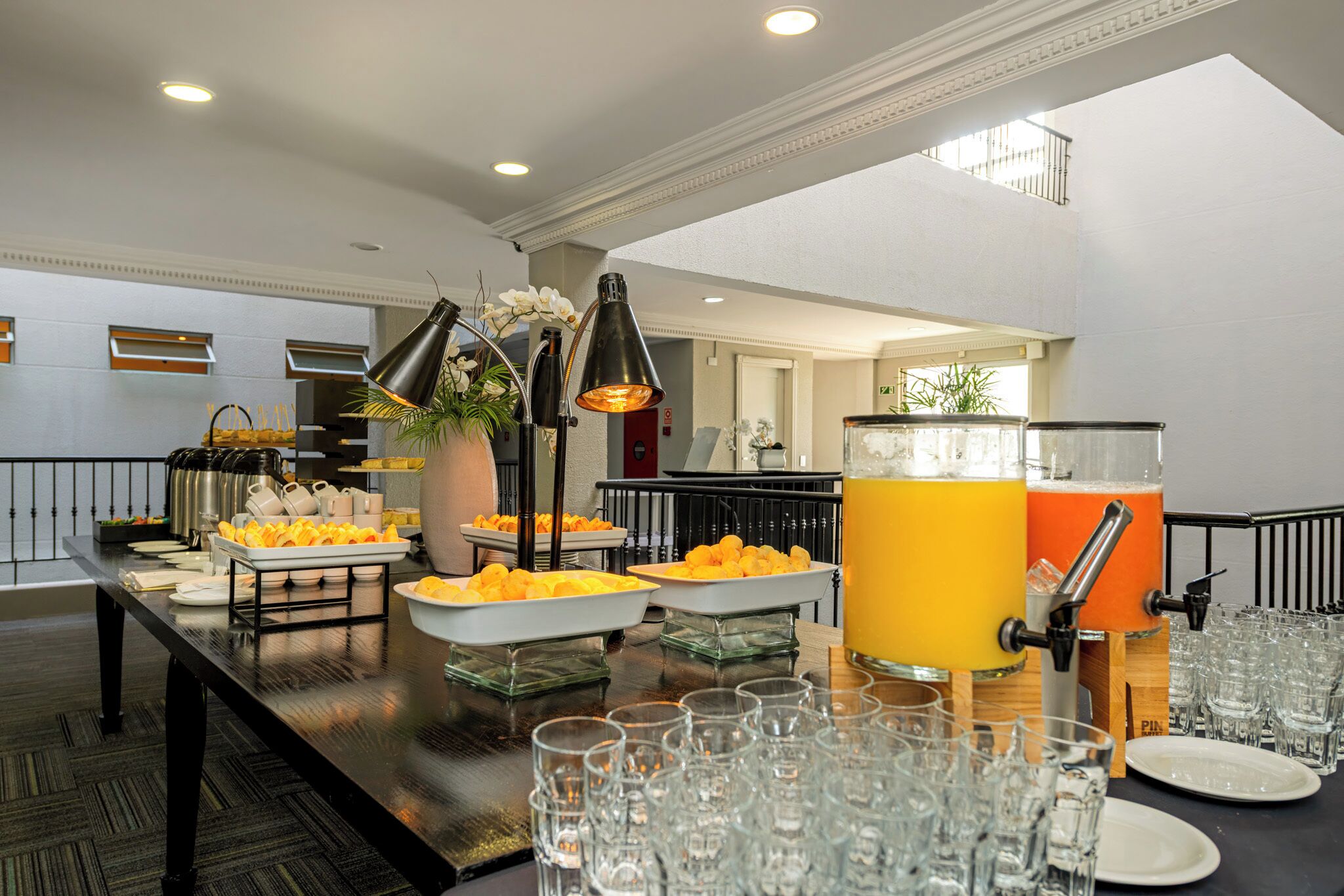 Un buffet proposant une variété de plats et un distributeur de jus, le tout entouré de verres et d’assiettes.