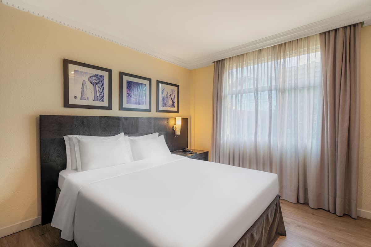 A hotel room with a large bed, a nightstand with a lamp, and three framed pictures on the wall.