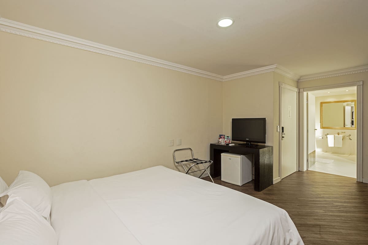 A hotel room with a bed, a television, a small refrigerator, and a bathroom visible through an open door.