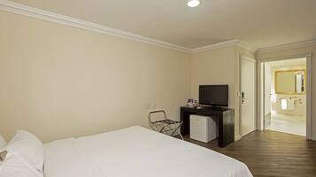 Habitación de hotel con cama, televisión, refrigerador pequeño y baño visible a través de una puerta abierta.
