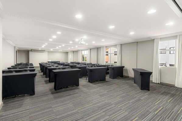 A conference room with rows of tables and chairs, large windows, and a carpeted floor. - Rockefeller by Slaviero Hotéis (Curitiba)