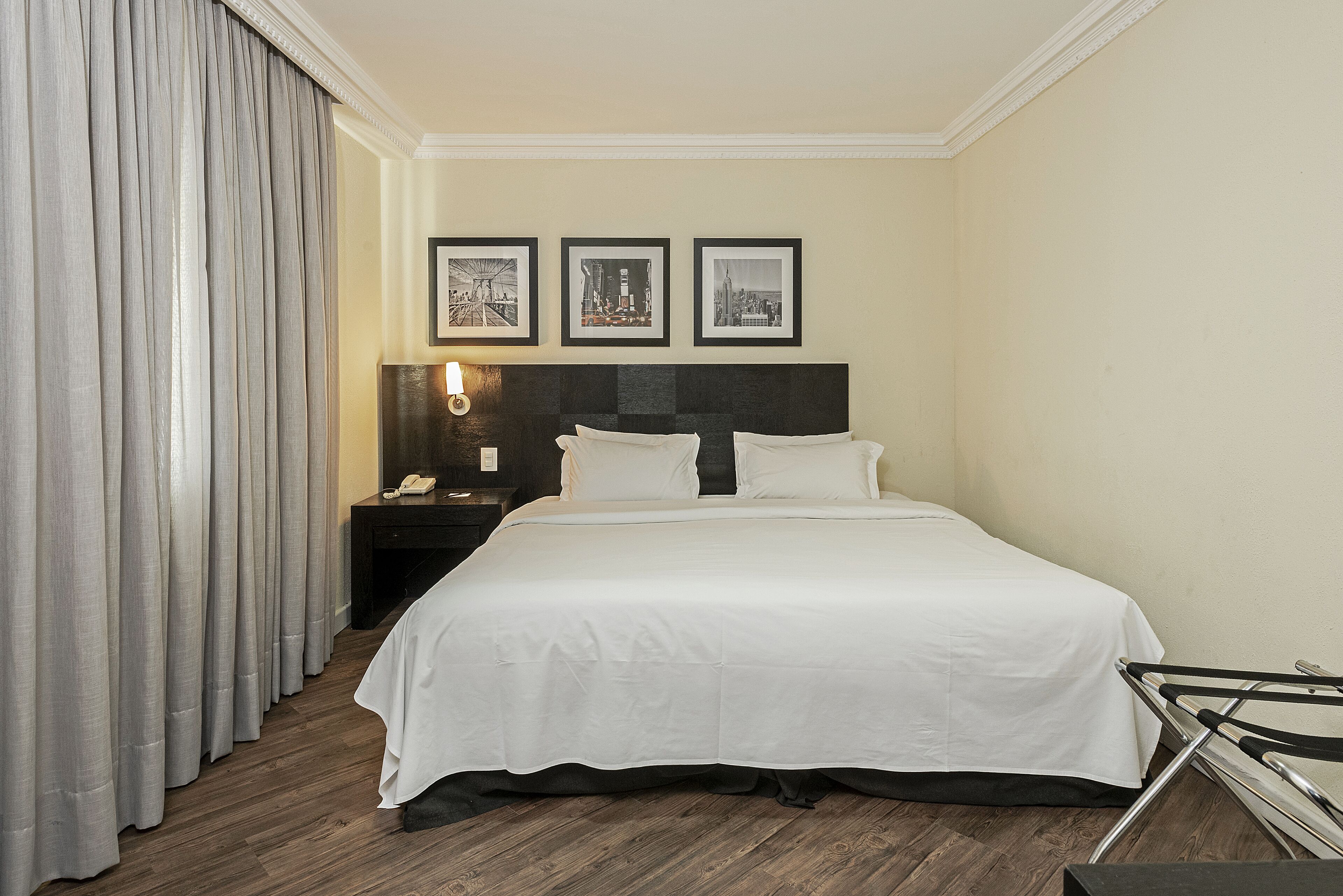 A hotel room with a large bed, a nightstand with a lamp, and three framed pictures on the wall.