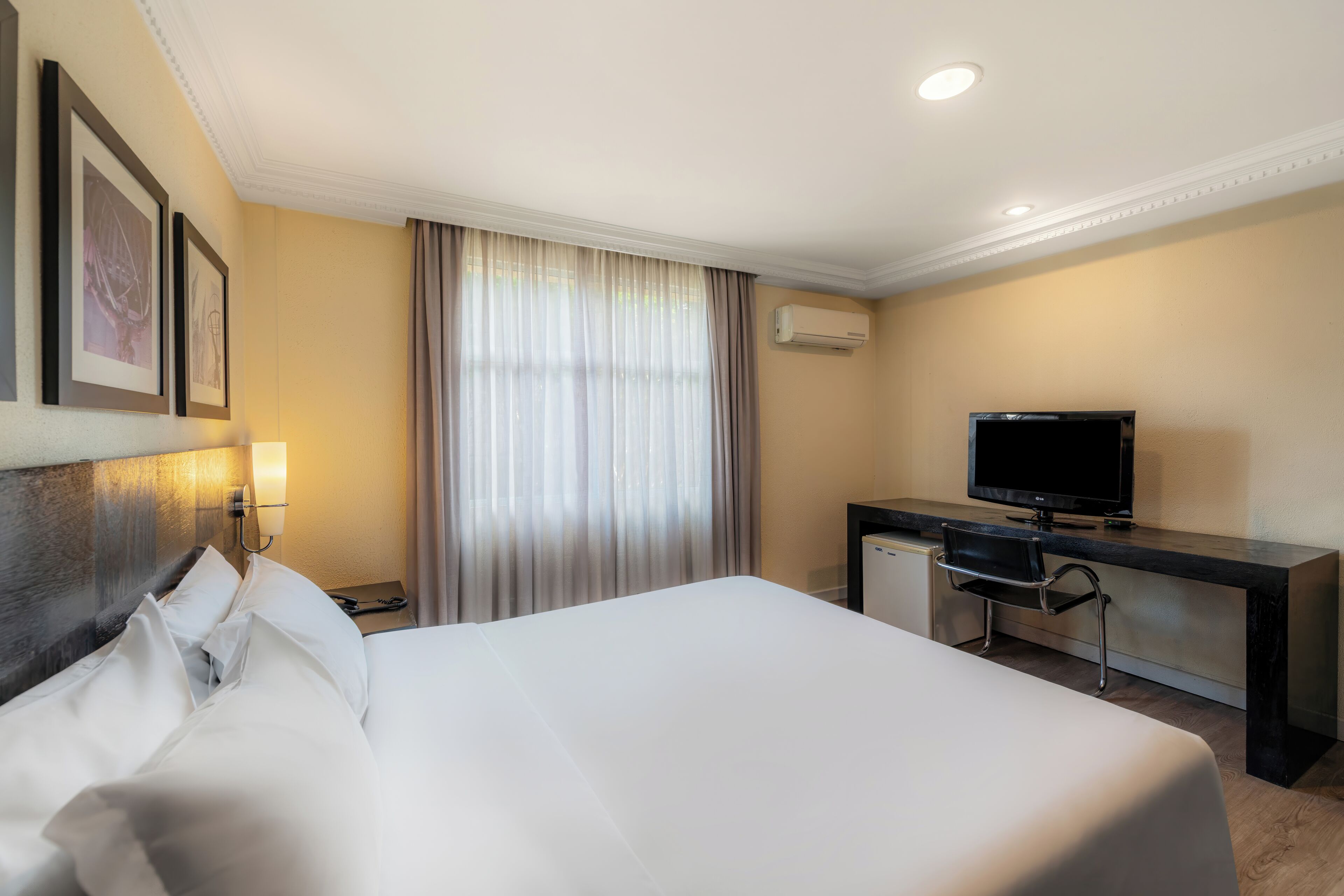 Une chambre d’hôtel avec un grand lit, un bureau avec une télévision, un appareil de climatisation et une fenêtre avec des rideaux.