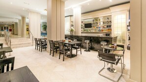 Un amplio vestíbulo de hotel con zona de bar, asientos y una escalera que conduce a otras plantas.