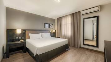 A modern hotel room with a large bed, bedside tables, a mirror, and an air conditioning unit.