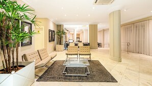 Un hall amplio con un sofá, dos sillones, una mesa de centro de vidrio y plantas en macetas.