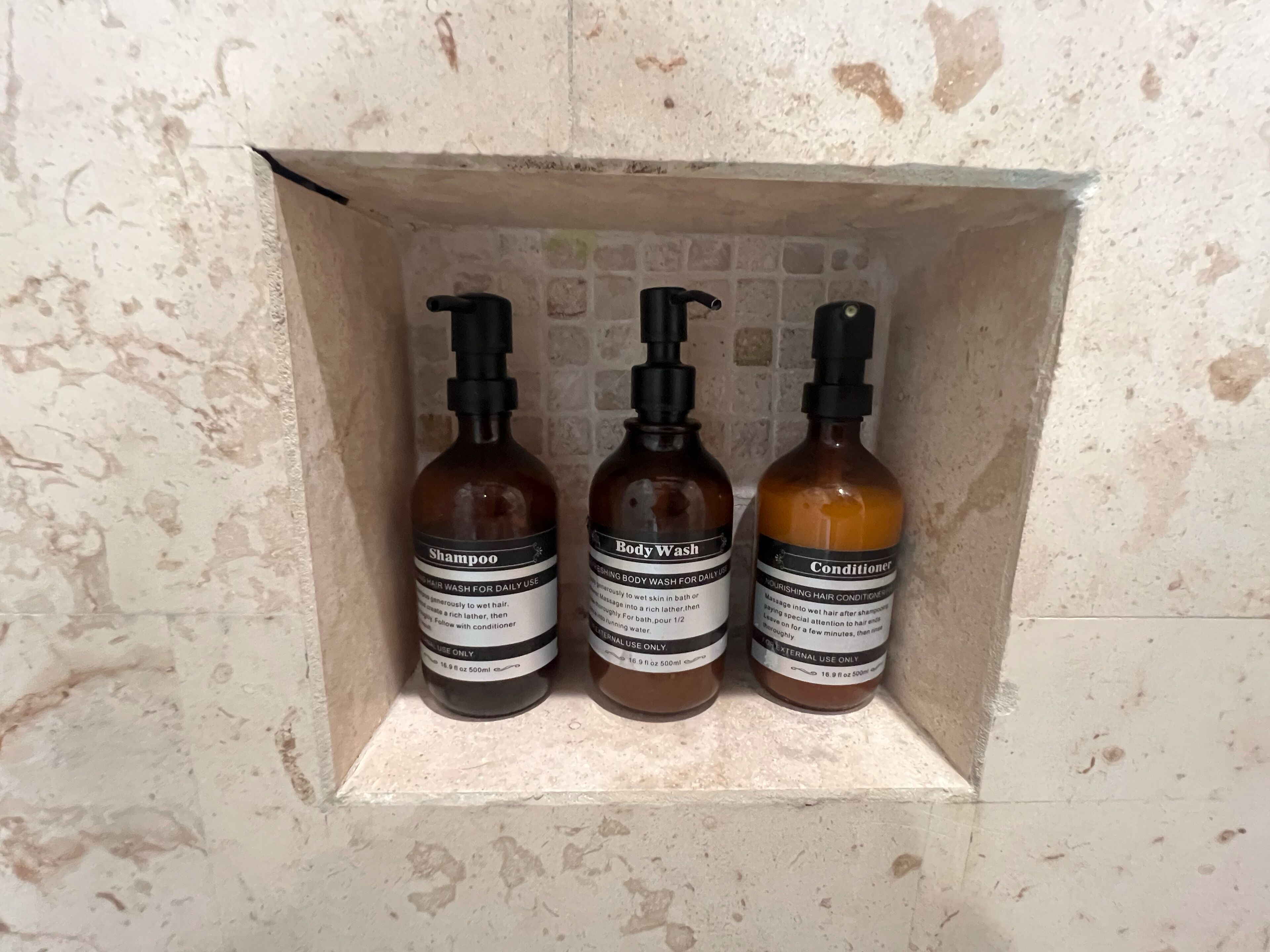 Three bottles of hair care products in a tiled niche.