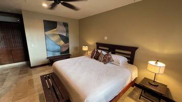 A bedroom with a large bed, a ceiling fan, a nightstand with a lamp, and a bench.