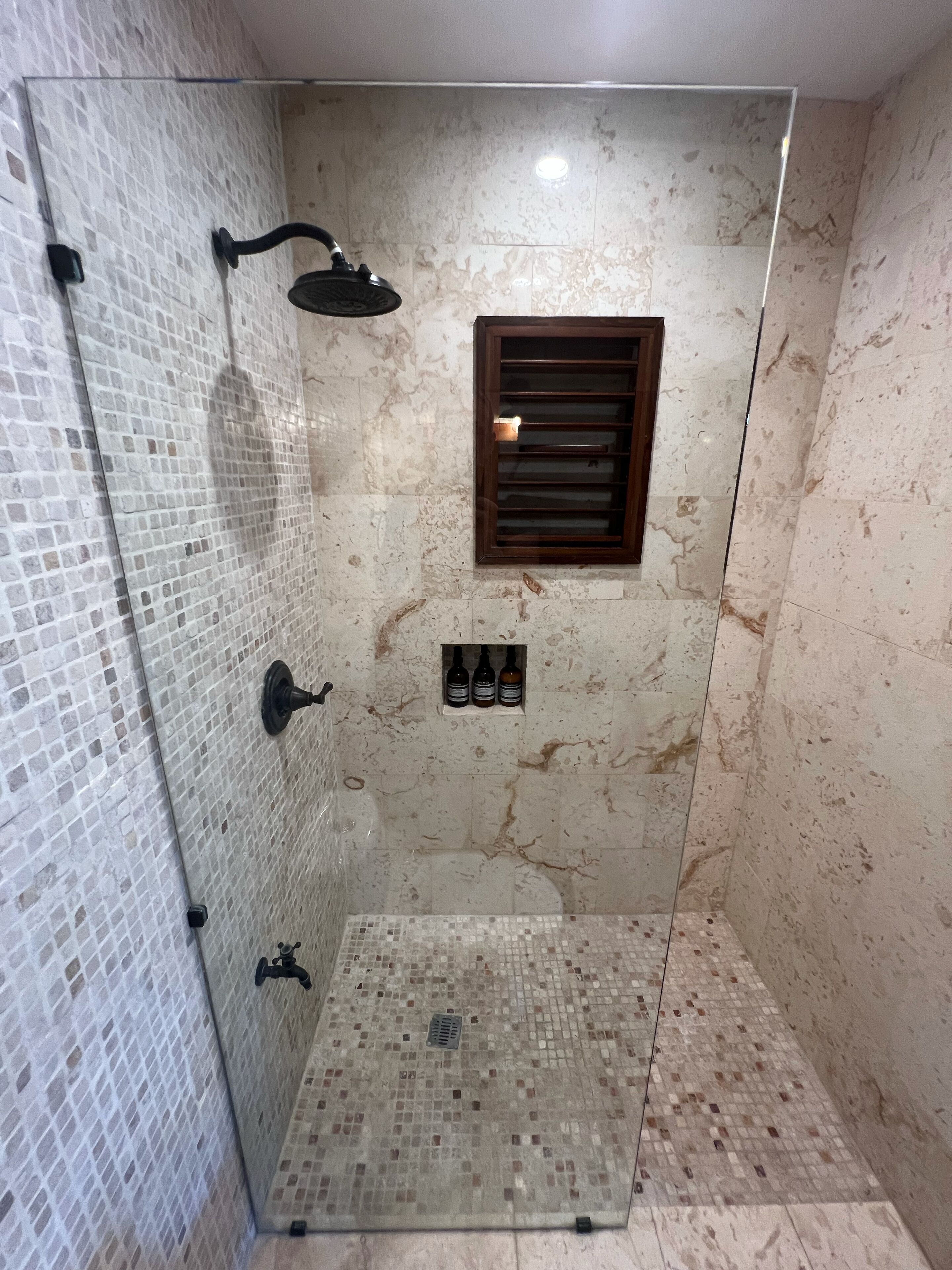 Een douche met een glazen deur, een handdouche en een klein plankje met flessen.