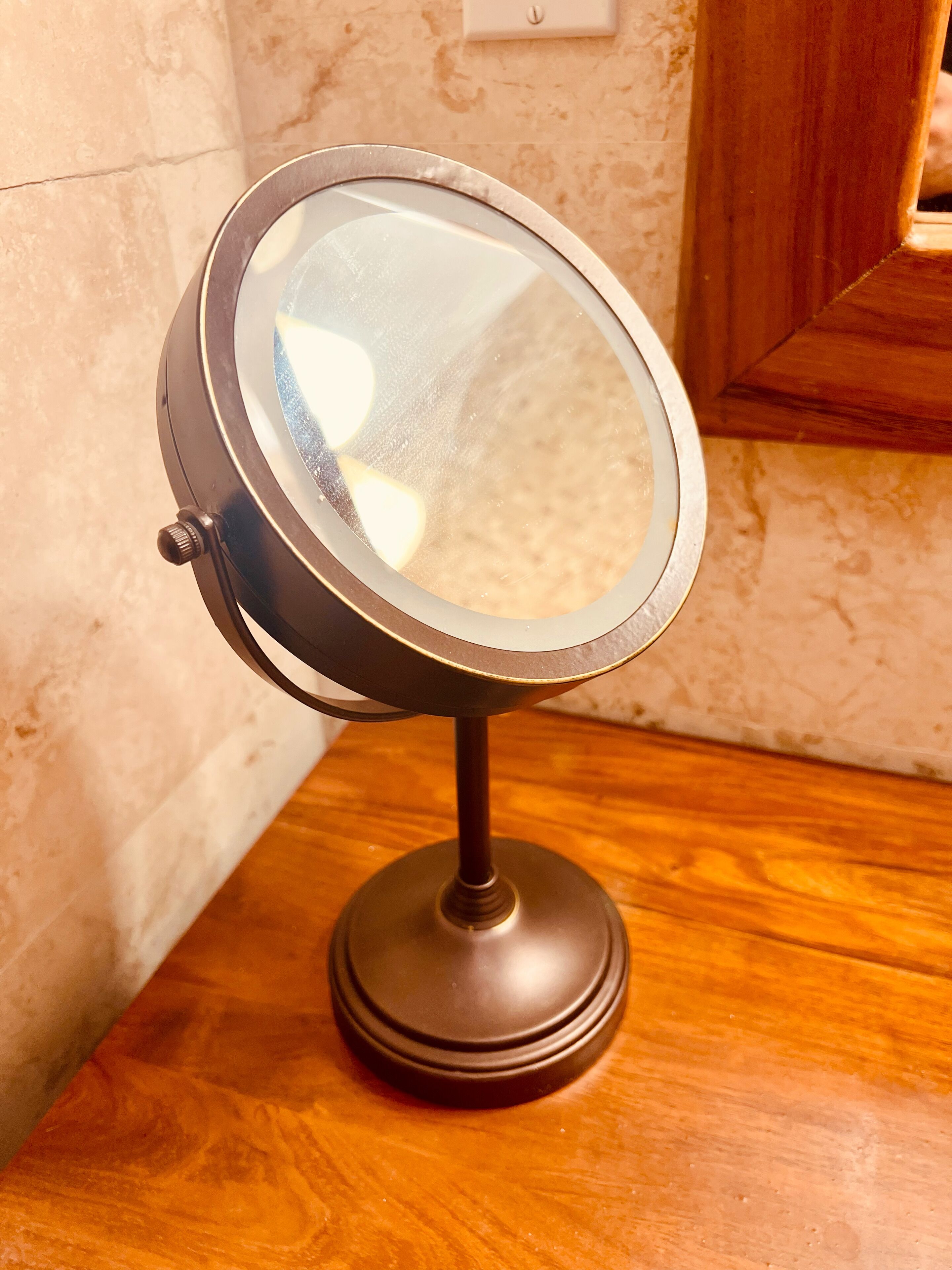 A round mirror with a metallic frame on a wooden table.