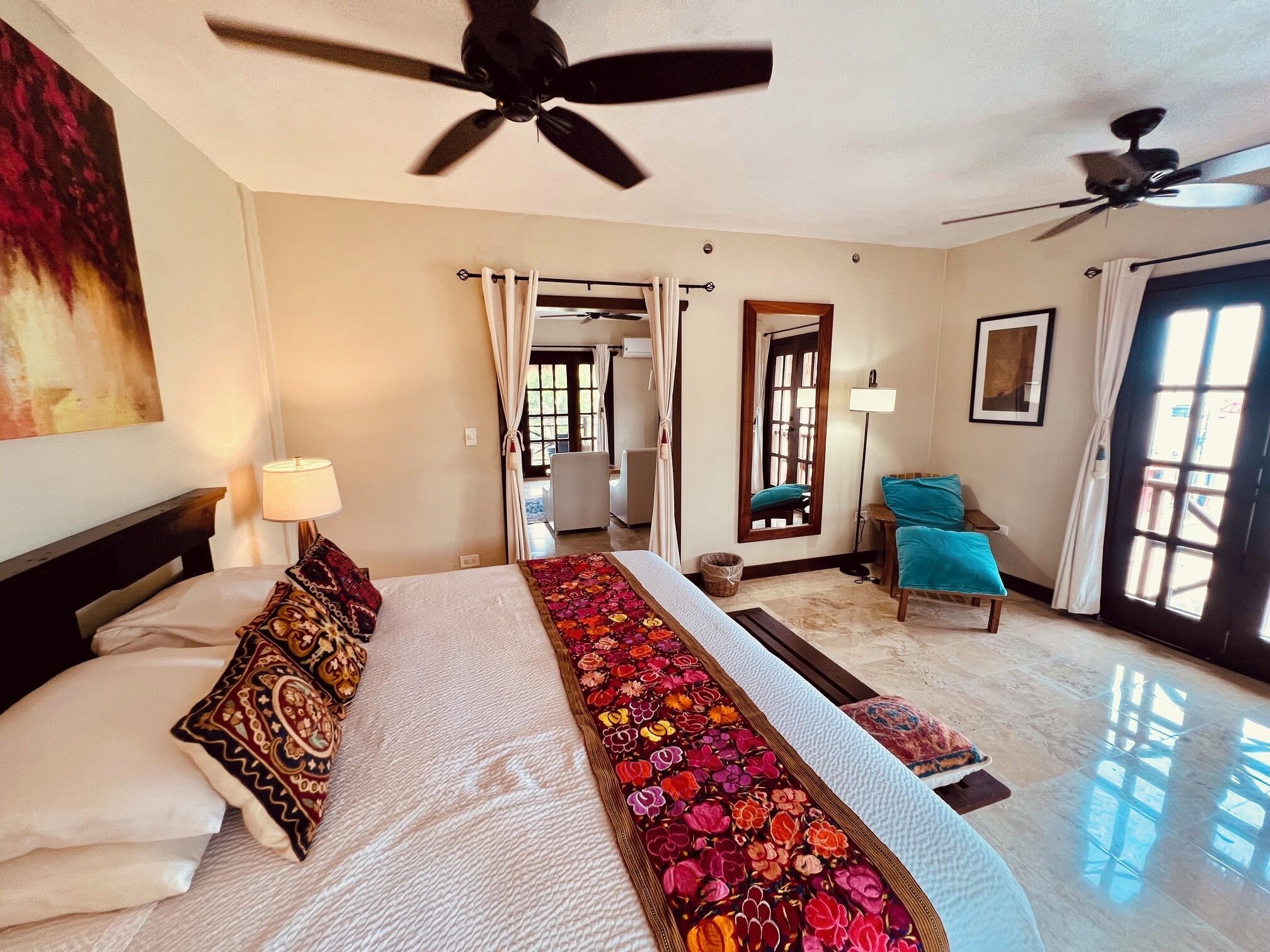 A hotel room with a bed, ceiling fans, a window, a door, and a chair.