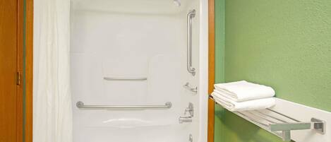 A bathroom with a bathtub, grab bars, a towel rack, and a toilet paper holder.