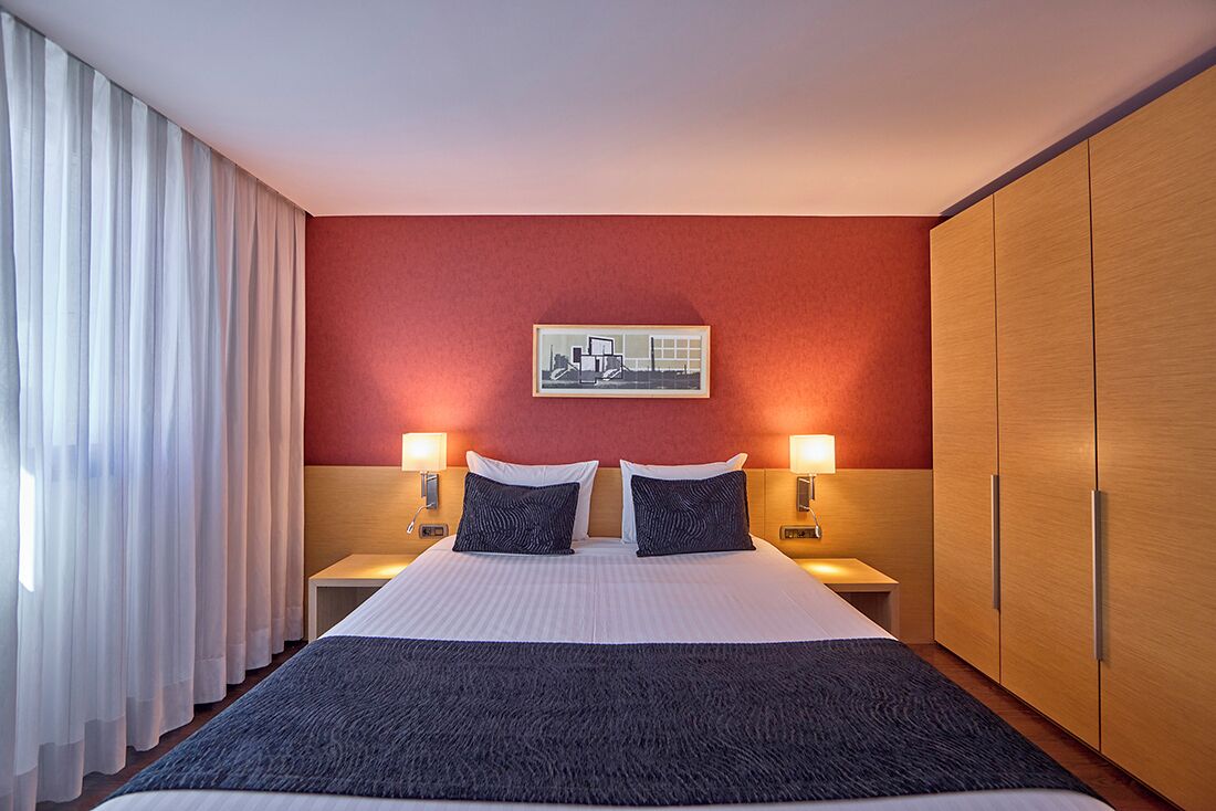 Une chambre d’hôtel avec un grand lit, deux tables de chevet avec des lampes, une armoire et un tableau encadré au mur.