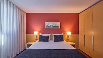 Une chambre d’hôtel avec un grand lit, deux tables de chevet avec des lampes, une armoire et un tableau encadré au mur.