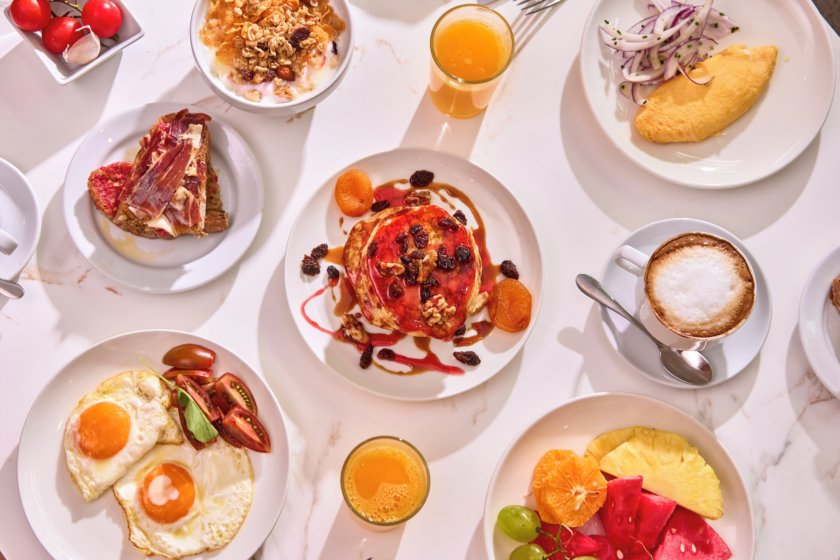 Un desayuno con diversos platos, entre ellos huevos, tostadas, fruta y bebidas.