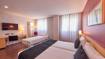 Une chambre d’hôtel avec un grand lit, un bureau, une chaise, une télévision et une fenêtre avec des rideaux.