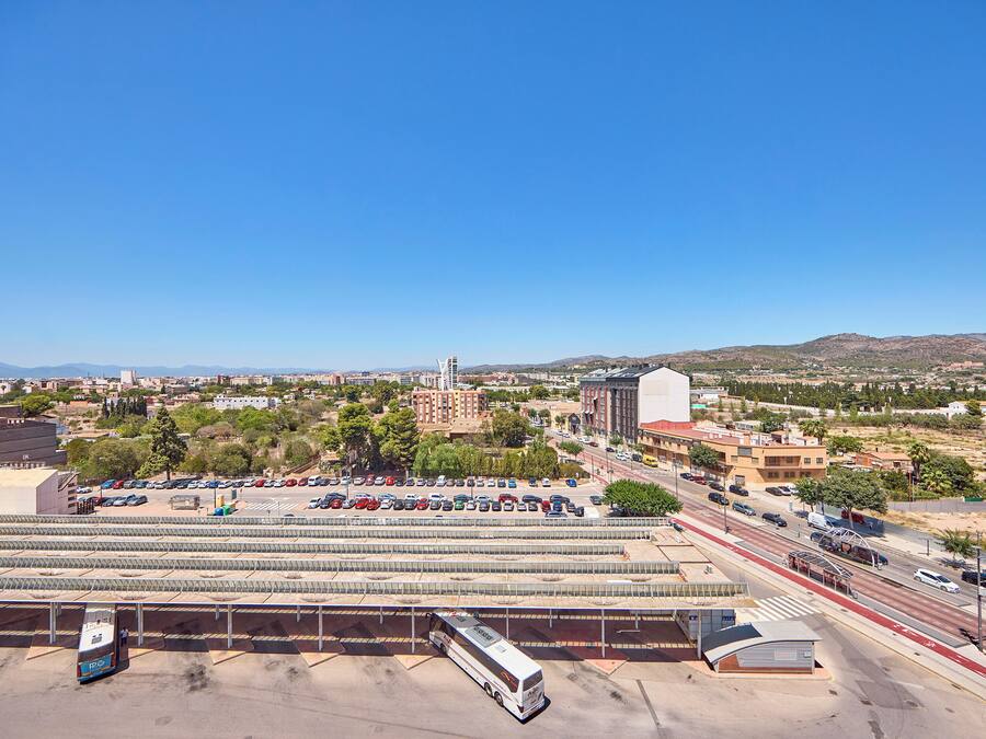 A bus station with multiple buses, a parking lot, and a view of a cityscape with buildings and hills.