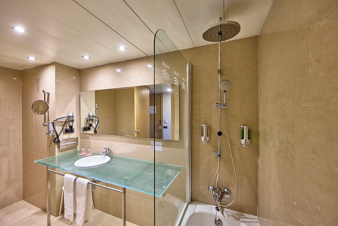 Een moderne badkamer met een glazen wastafel, een grote spiegel, een douche met regendouche en een bad.