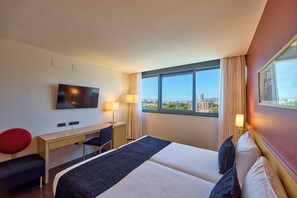 Habitación de hotel con cama, escritorio, silla, televisor y un ventanal con vista a la ciudad.