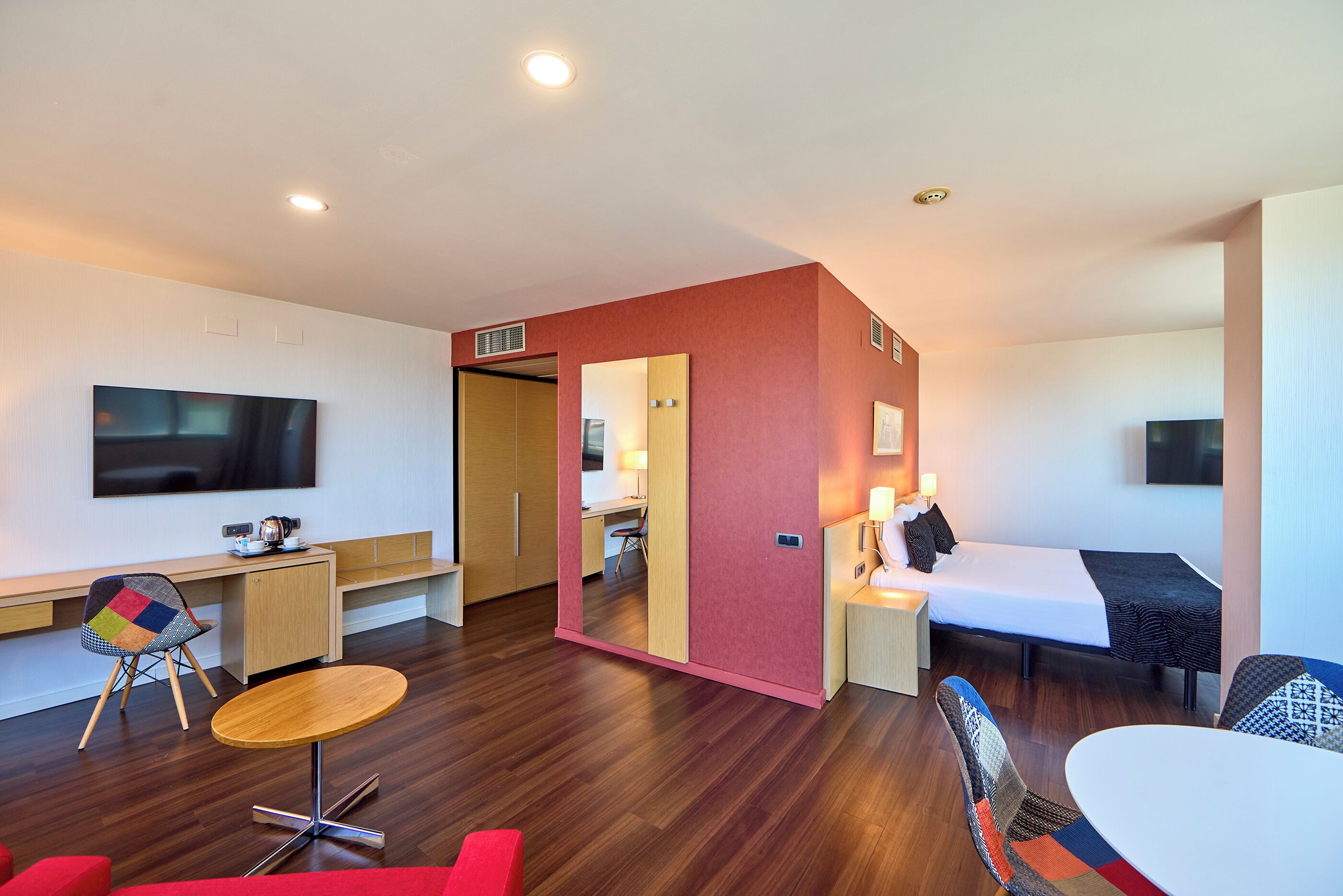 Una habitación de hotel moderna con un escritorio de madera, una televisión, una cama y un pequeño comedor.