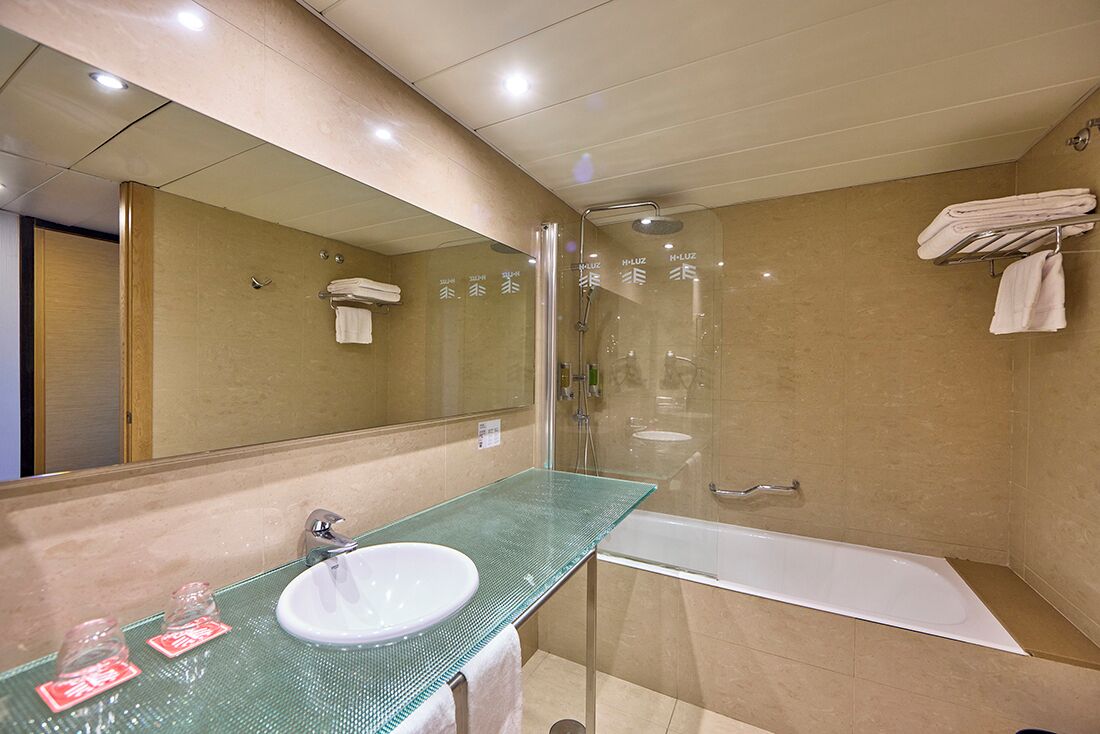 A modern bathroom with a glass sink, a large mirror, a glass-enclosed shower, and a white bathtub.