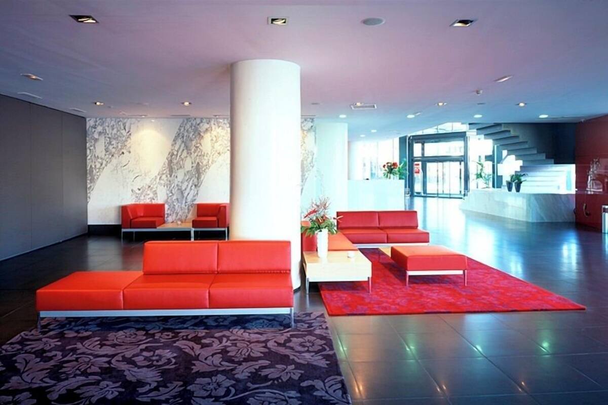 A modern lobby with a large central column, red seating, a patterned rug, and a marble wall.