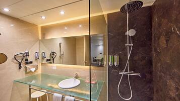 Un baño moderno con un lavabo de cristal, un cabezal de ducha de mano y un espejo grande.