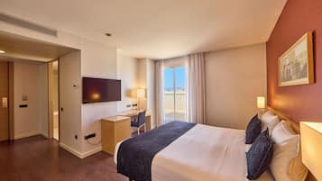 Habitación de hotel con una cama grande, un escritorio, una silla, un televisor y un balcón con vistas.