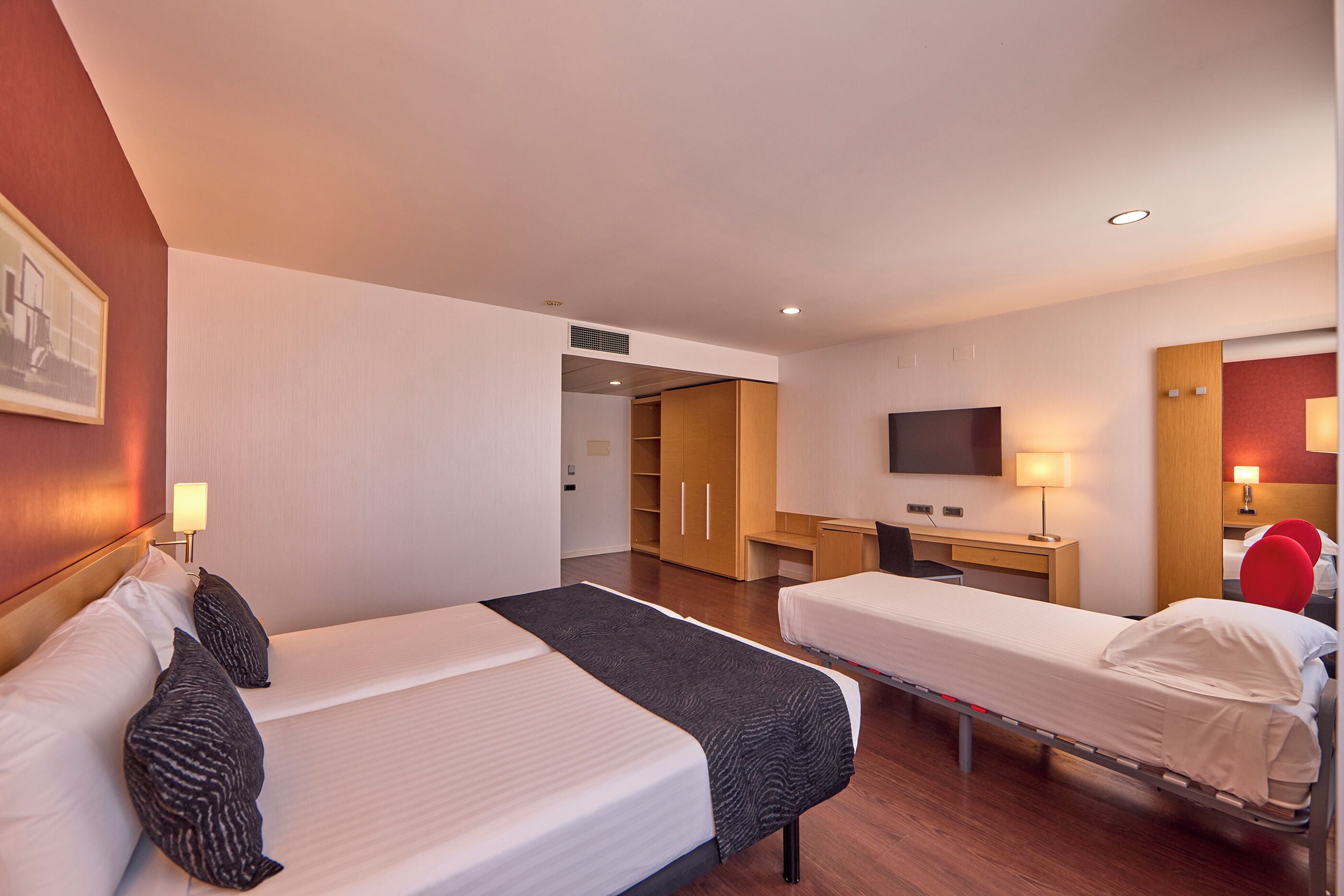 Habitación de hotel con dos camas, un escritorio, un televisor y un armario.