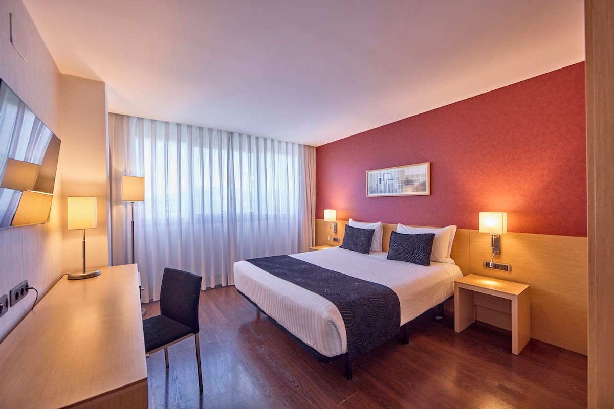 Hotellihuone, jossa on suuri sänky, yöpöydät lampuineen, työpöytä ja tuoli.