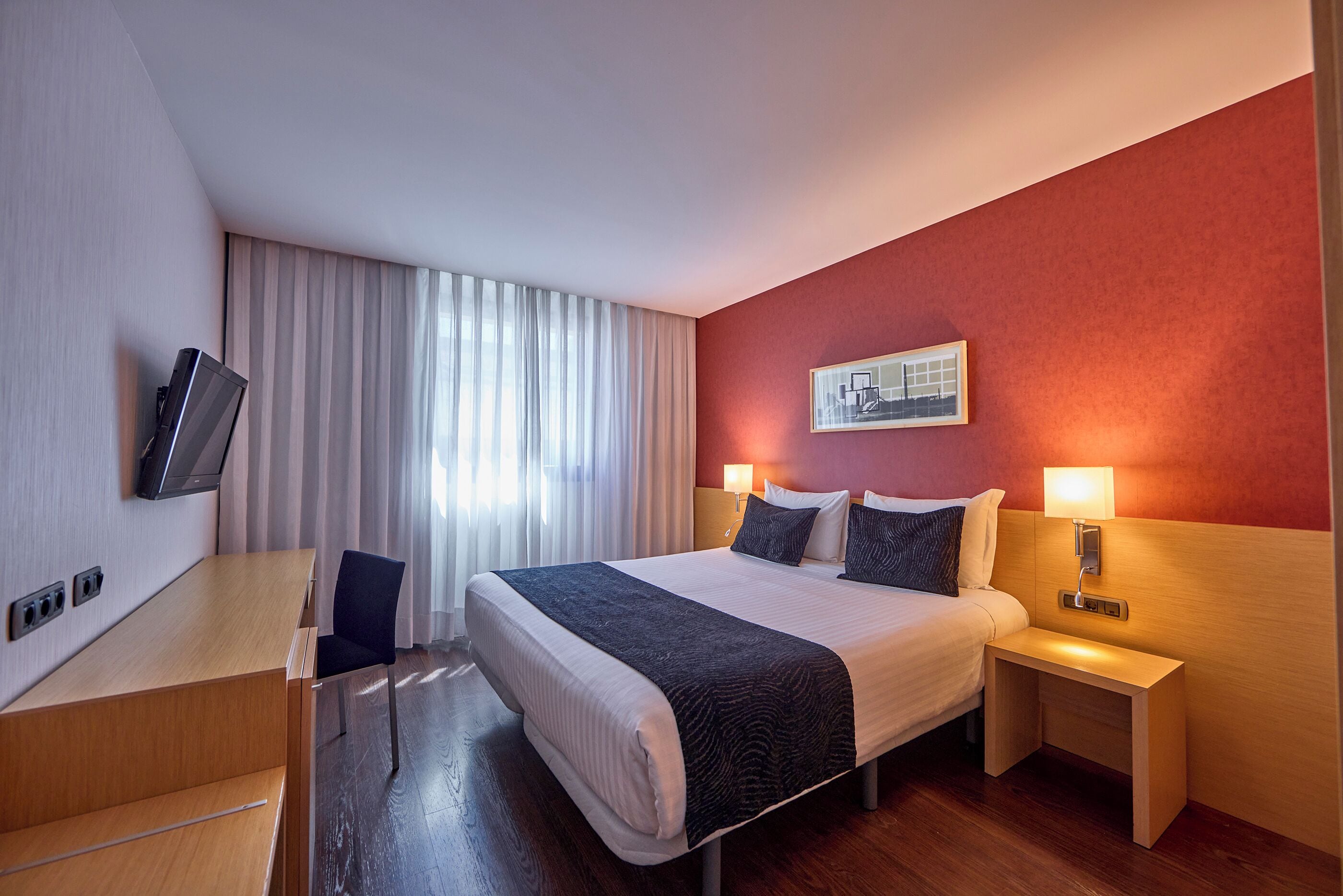 A hotel room with a bed, bedside lamps, a desk, and a television.