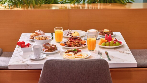 Un bufé de desayuno con diversos platos, bebidas y una zona de estar con vistas a zonas verdes.