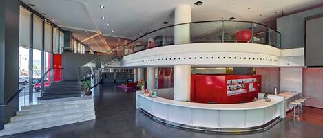 A spacious lobby with a curved reception desk, a staircase, and a glass railing on the upper level.