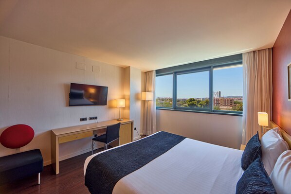 Quarto de hotel com uma cama grande, escrivaninha, cadeira, televisão e janela com vista para a cidade.