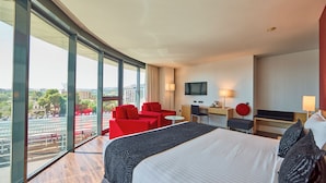 Una habitación de hotel con una cama grande, sillas rojas, un escritorio y un televisor.