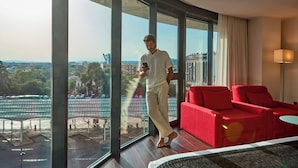Habitación de hotel con un ventanal grande, sofá rojo y vistas a un paisaje urbano.