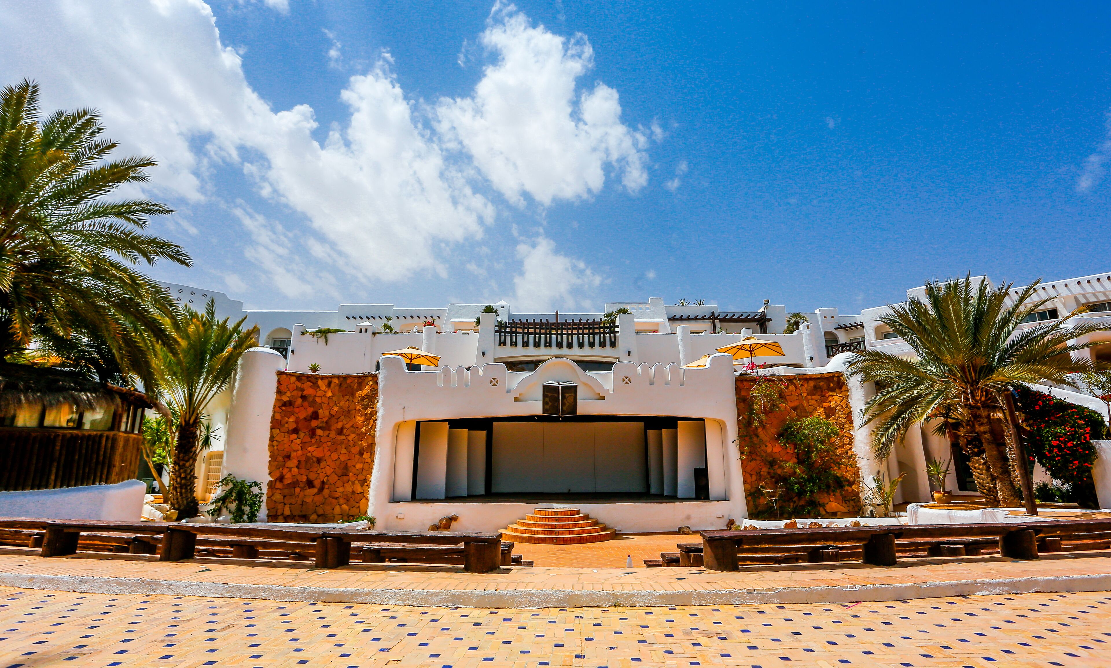 A building with a white facade, a central entrance with steps, and palm trees around.