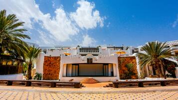 A building with a white facade, a central entrance with steps, and palm trees around.