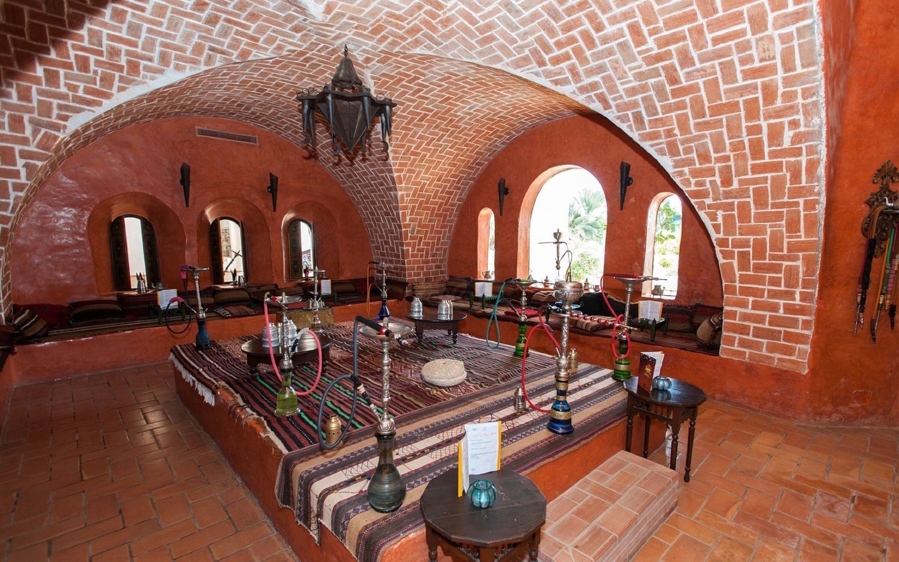A traditional interior with brick arches, a central seating area with cushions, and a variety of hookahs.