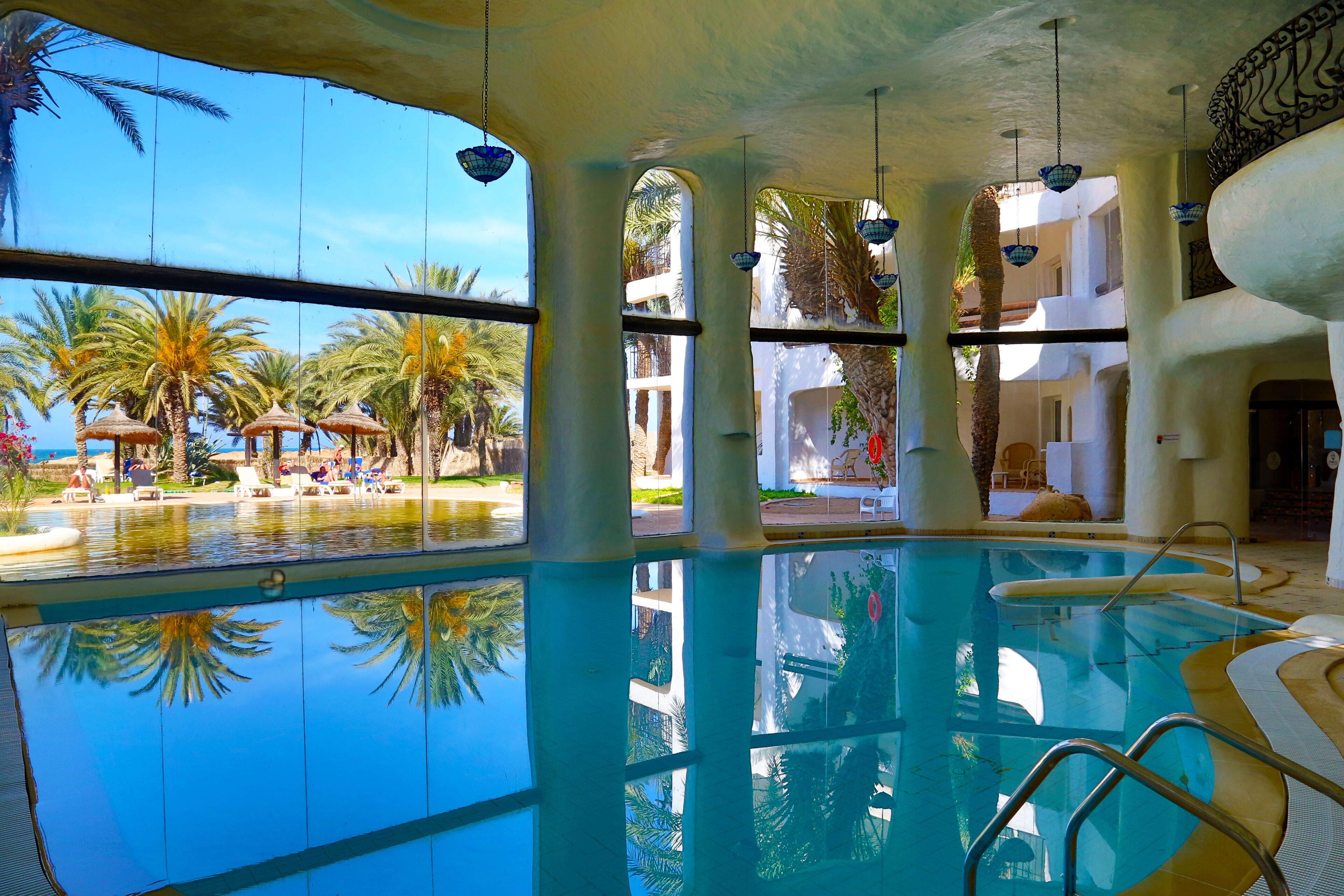 An indoor swimming pool with clear views of palm trees and a poolside area.