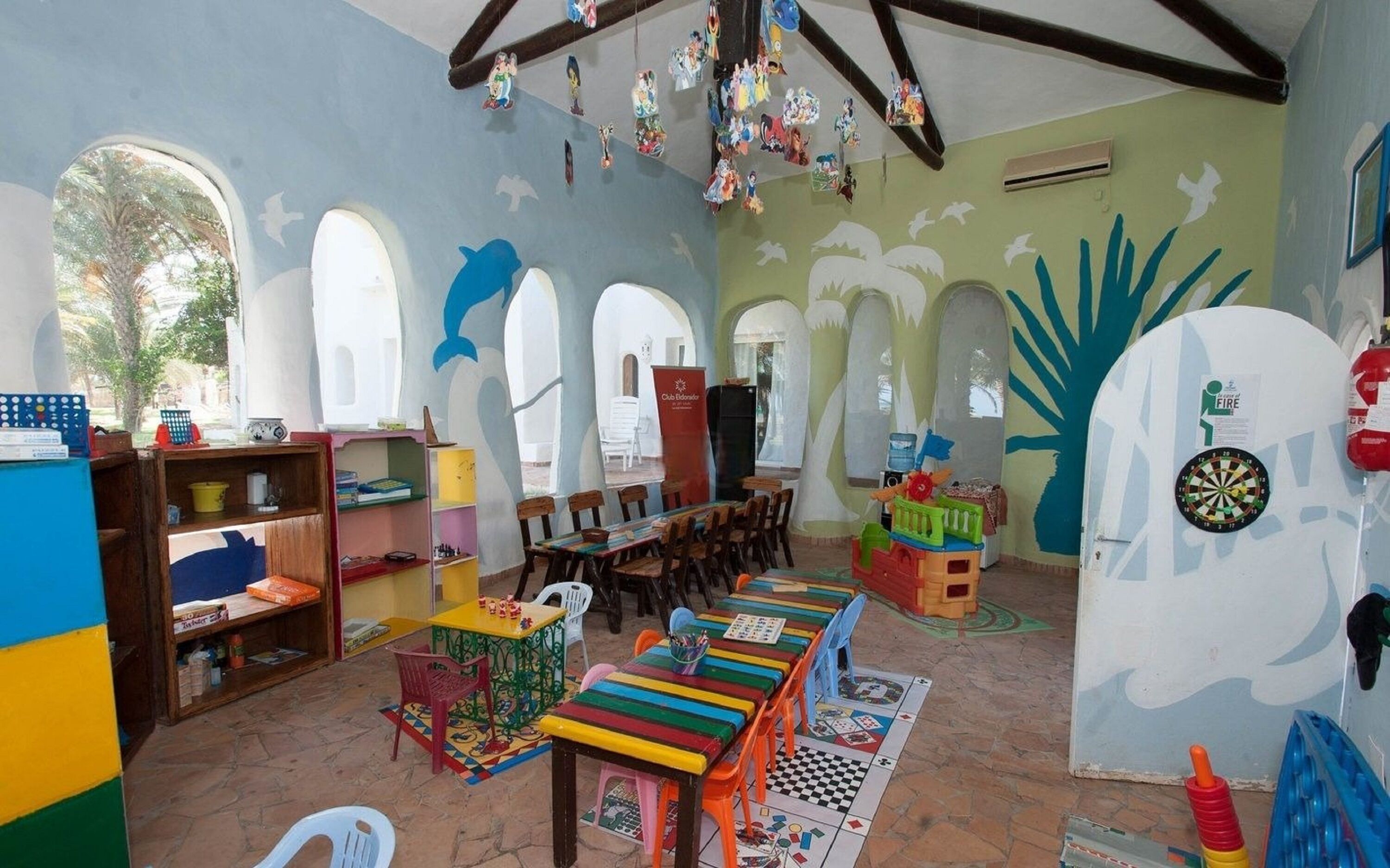 A colorful children's playroom with a long table, chairs, and various toys.