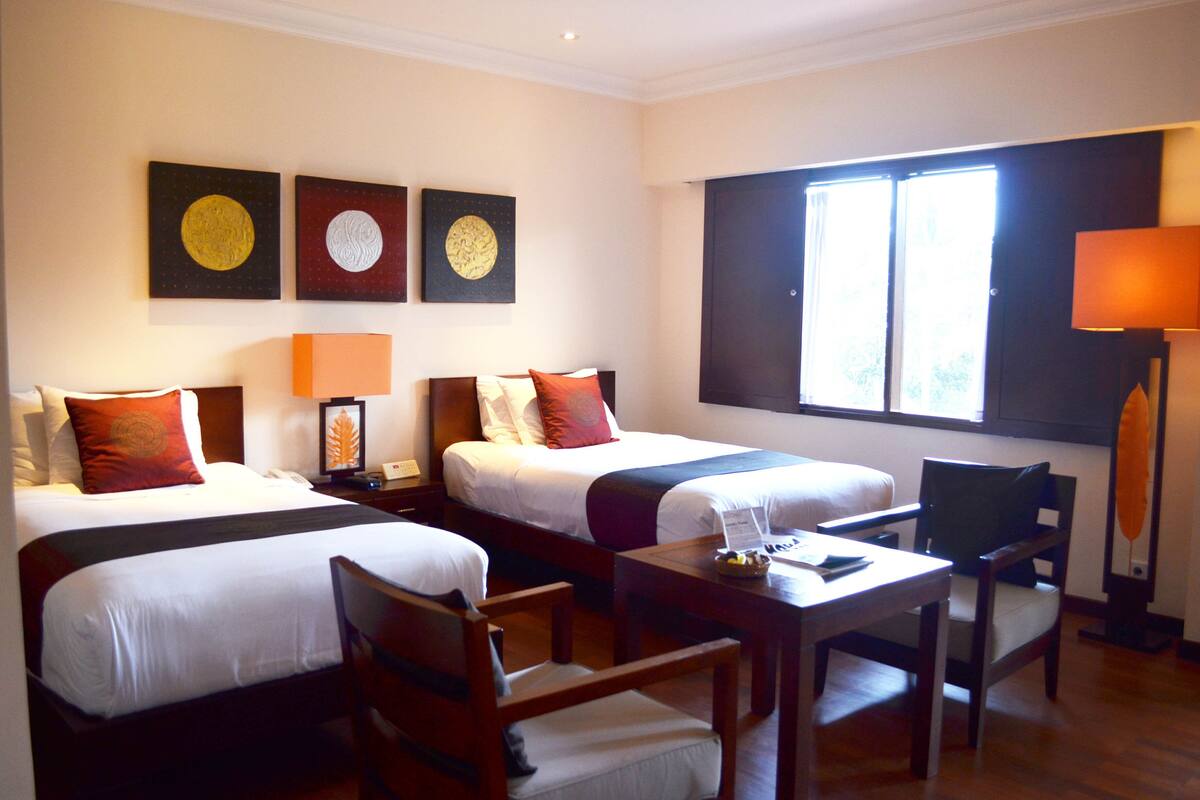 A hotel room with two beds, a desk, chairs, and artwork on the wall.