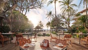 An outdoor dining area with wooden tables and chairs, a menu board, and a view of the ocean.