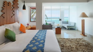 Una habitación de hotel moderna con una cama grande, vistas al océano, un balcón con asientos y un cabecero de madera.
