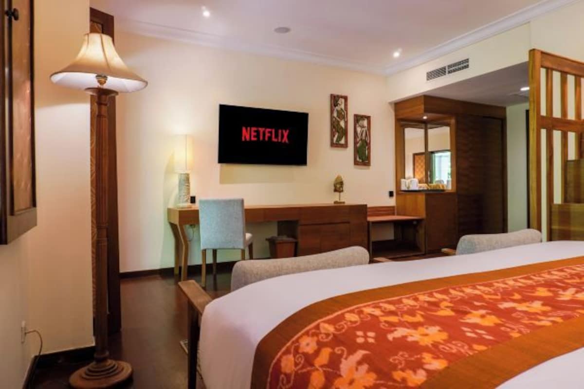 Habitación de hotel con cama, escritorio, silla, lámpara y televisor mostrando el logotipo de Netflix.