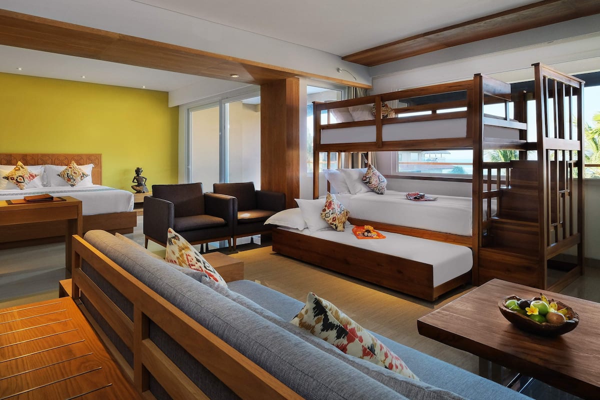 A modern hotel room with a bunk bed, a sofa, a desk, and a dining table.