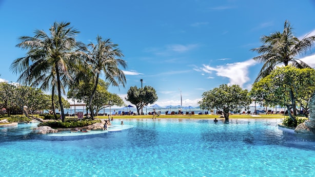 Una piscina azul cristalina rodeada de palmeras y sillas de descanso, bajo un cielo despejado.
