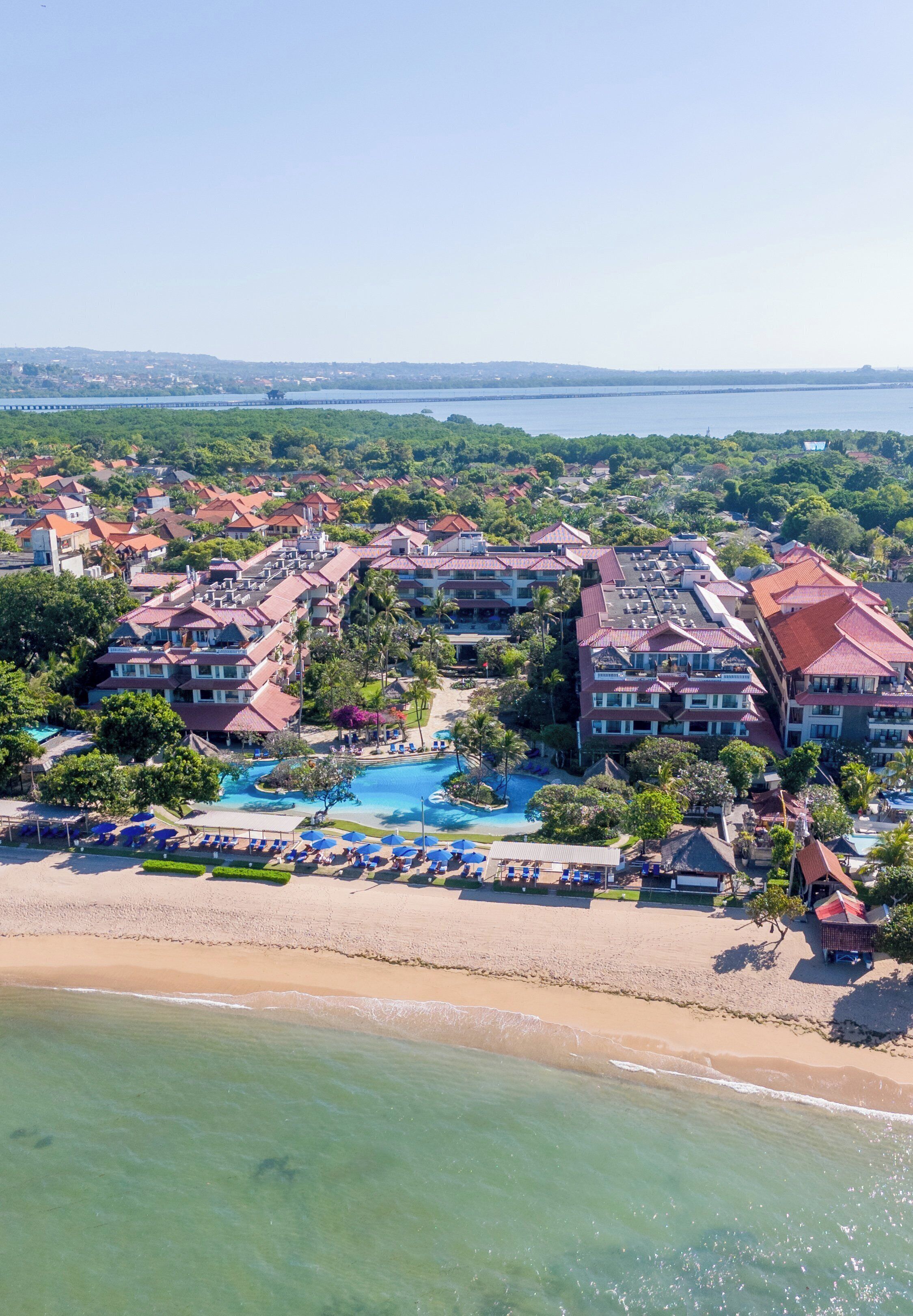An aerial view of a resort with multiple buildings, a large swimming pool, and a beach.